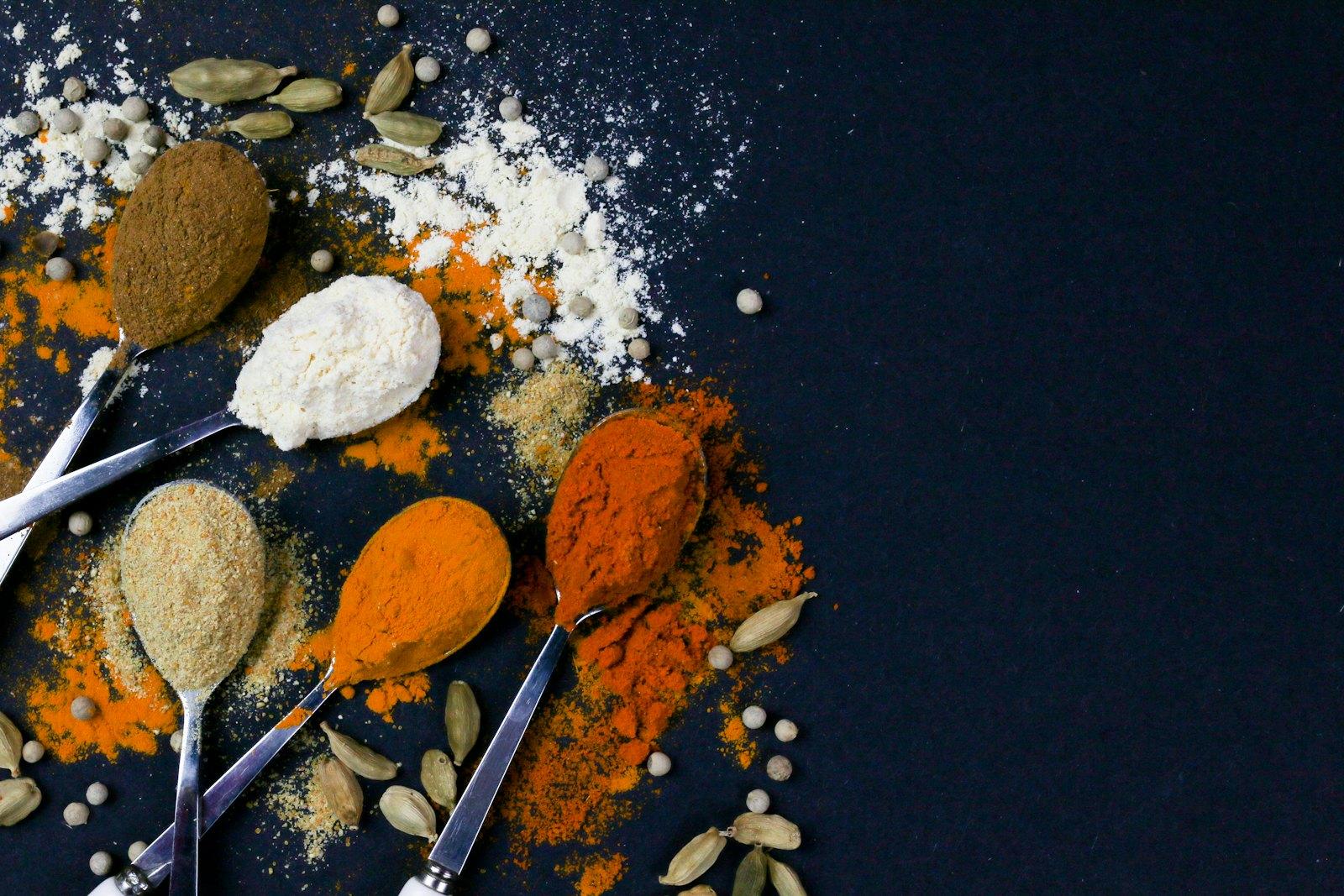 Spoons of ground turmeric and spices on a dark surface